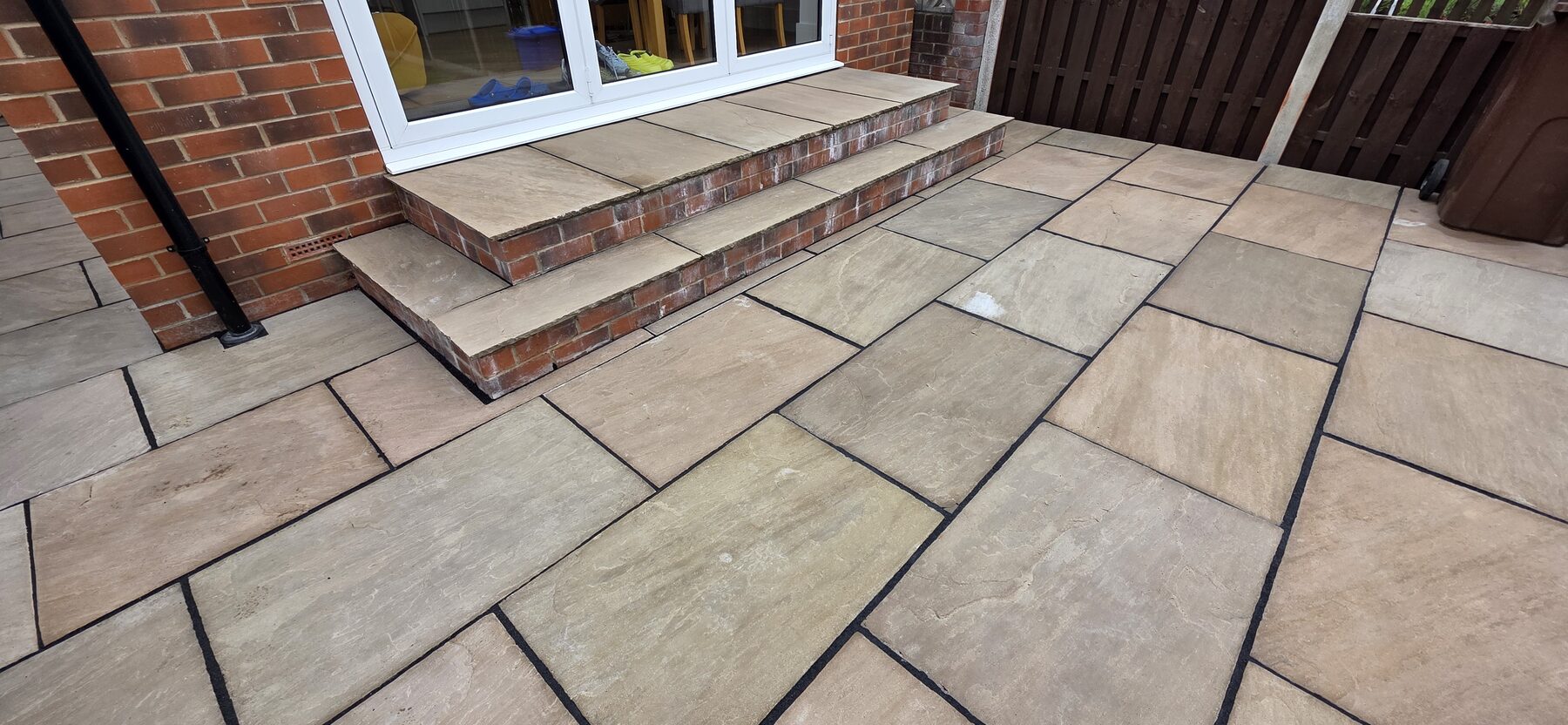 Completed stone patio with matching wide steps beside the house